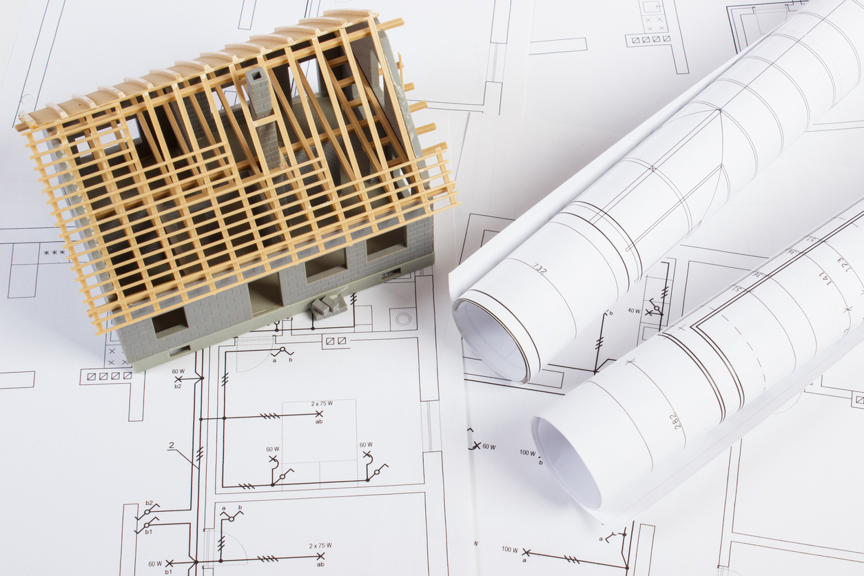 Multiple floor plan blueprints sit below a model of a custom home, allowing the homeowner to visualize what the house will look like once completed.