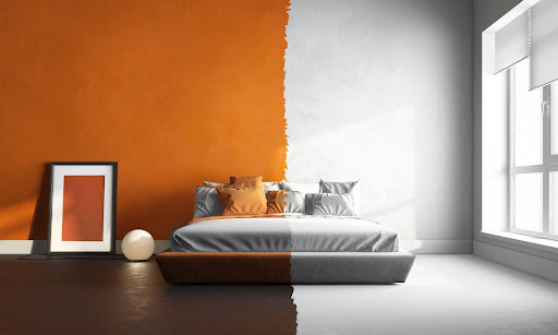 A bedroom is shown with one half painted a burnt orange color, complemented by dark wood floors, while the other half is white and bland.